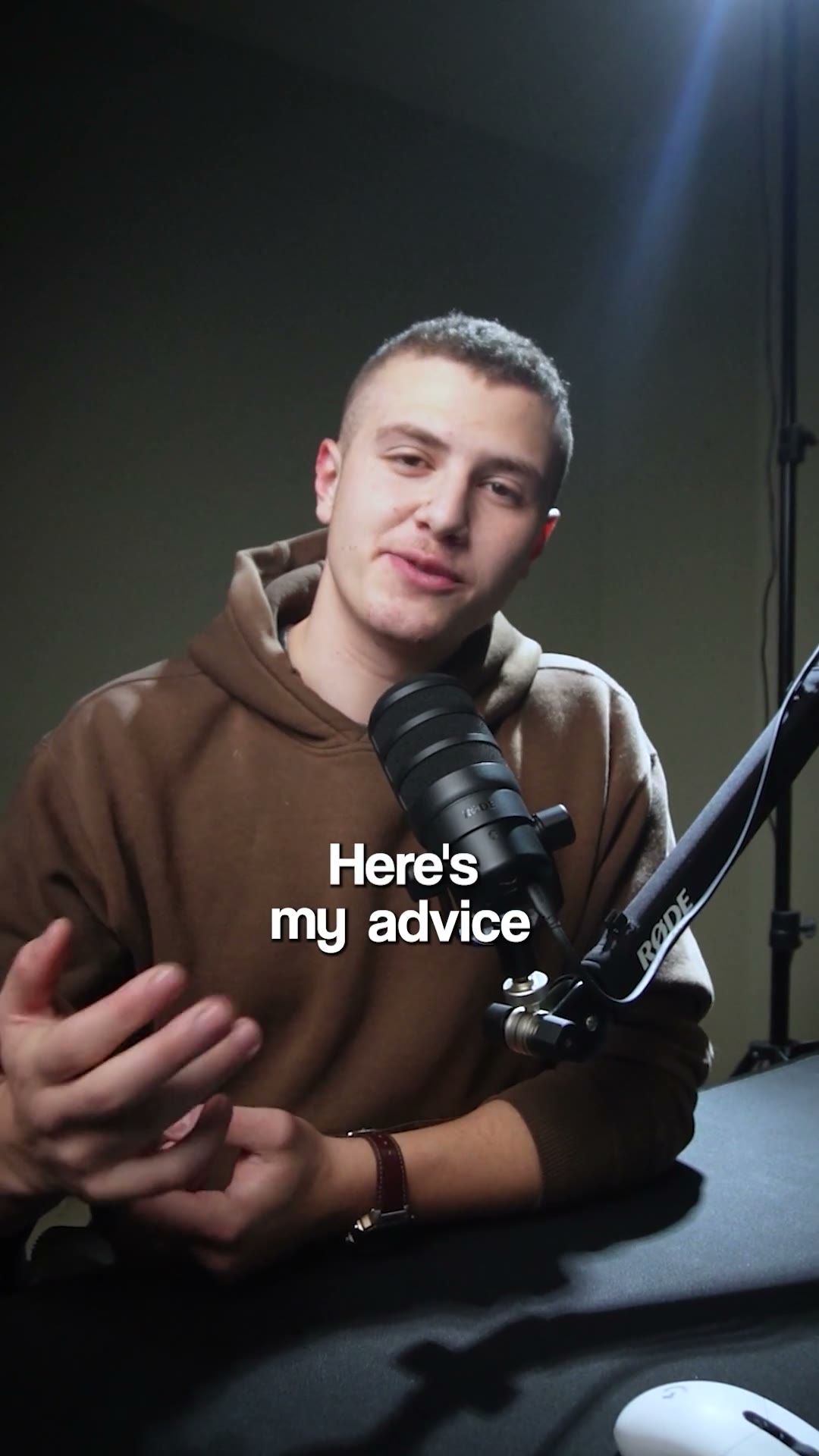 A young man in a tan hoodie talks to camera behind a broadcast mic, a blue rim light on the grey backdrop behind him and “Here’s my advice” set in white over his hands.